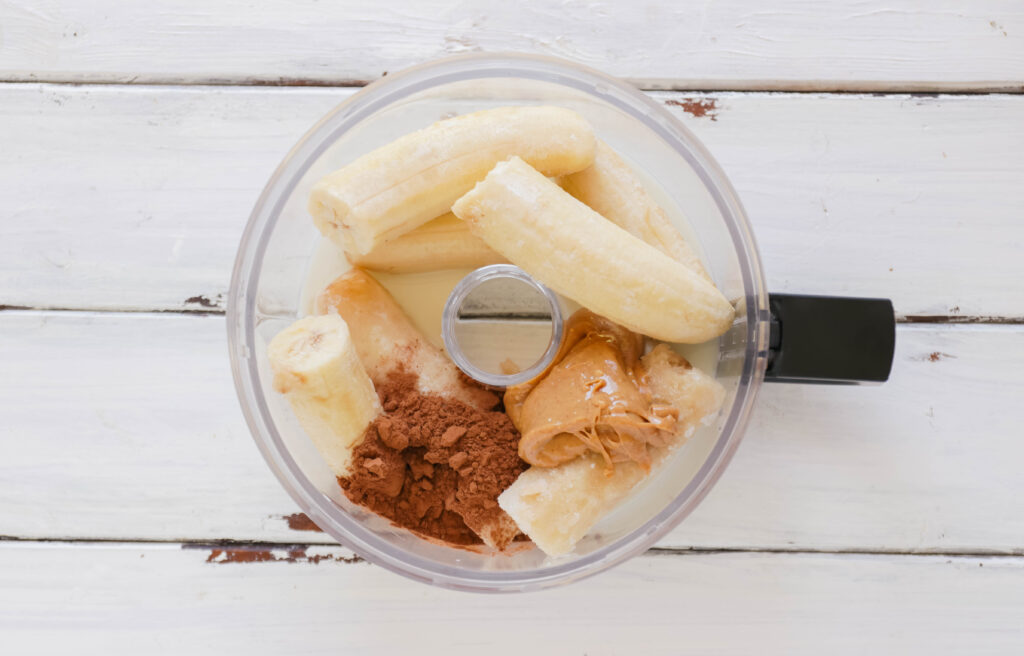 Food processor with ingredients for Chocolate Peanut Butter Ice Cream Cups; Vegan, dairy free and gluten free banana ice cream bites packed with cocoa and PB flavours.