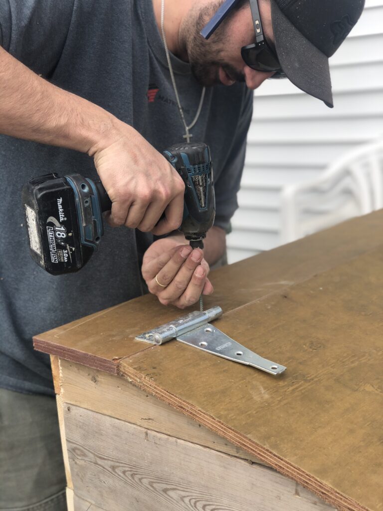 Close up of Drilling hinges onto outdoor garbage box lid for easy opening