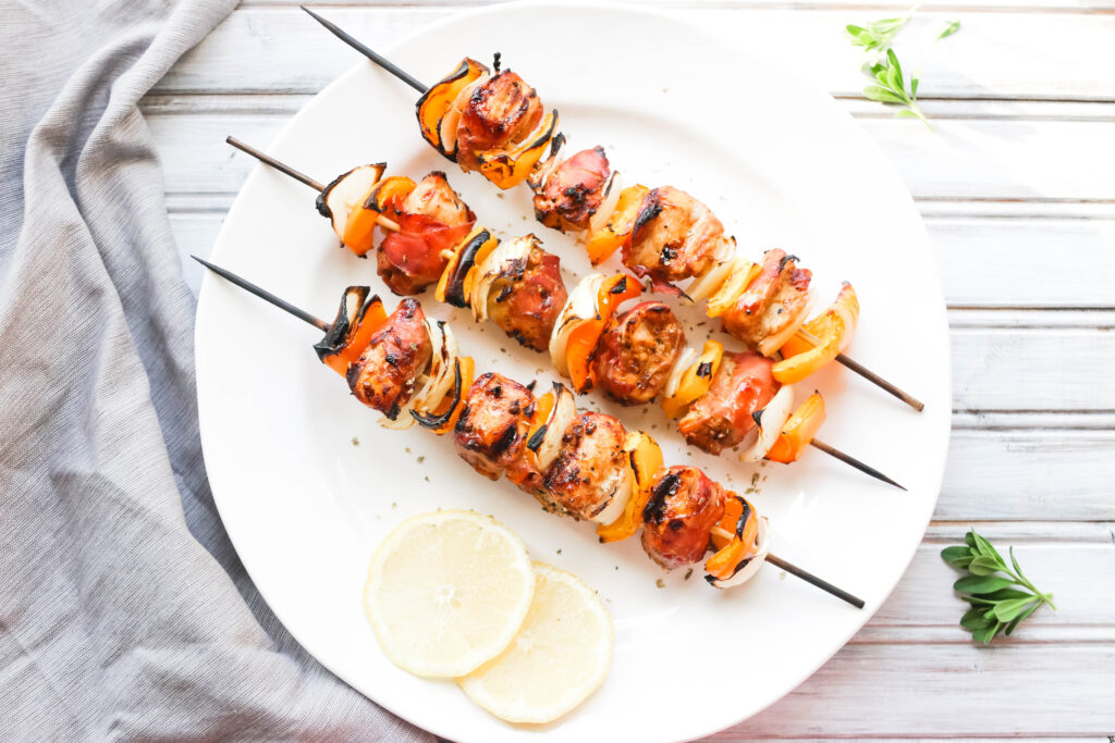 This Prosciutto Wrapped Chicken Skewers recipe is a quick and easy BBQ dinner that is bursting with salty goodness and juice peppers and onions. || Nikki's Plate