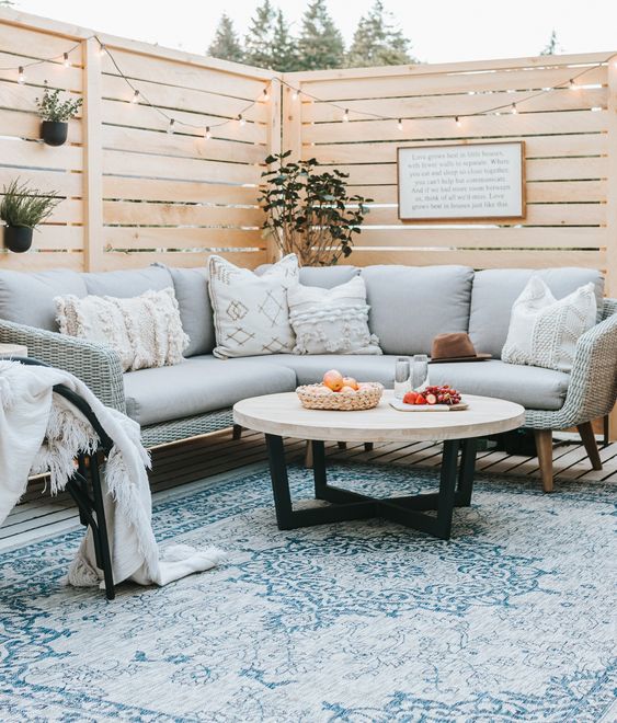 15 Deck Must Haves for Summer Entertaining; comfy sectional, comfy seating coffee table, blue outdoor rug, privacy wall with lights