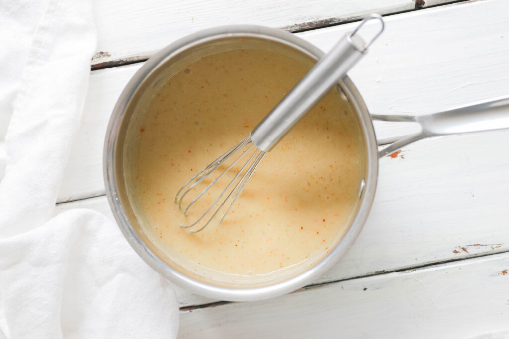 Sauce pot with whisk. White cheese sauce inside Vegan