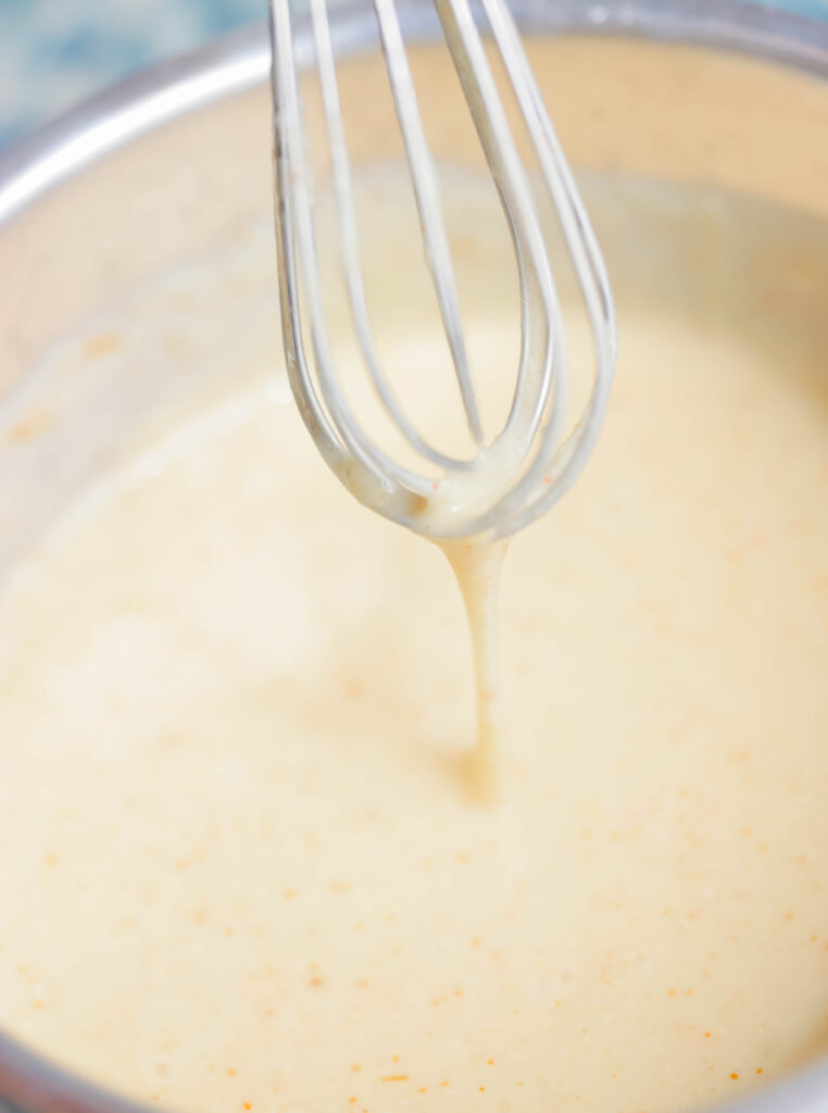 Sauce pot with whisk. White cheese sauce inside Vegan