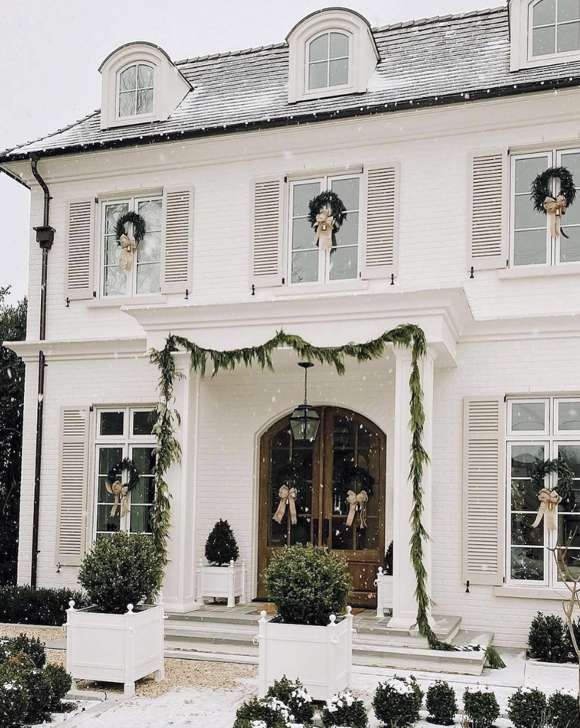 Classic winter front porch decor with evergreen garlands, wreaths with neutral bows, and a white brick exterior