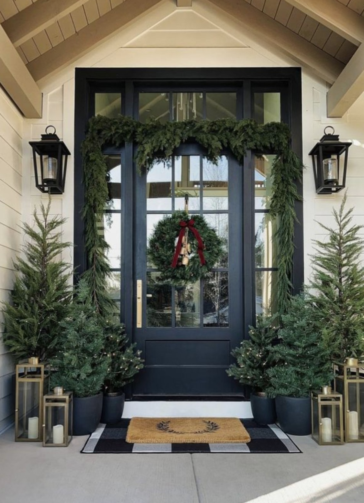 Farmhouse winter front porch decor with evergreen garland, matching planters, lanterns, and a black front door