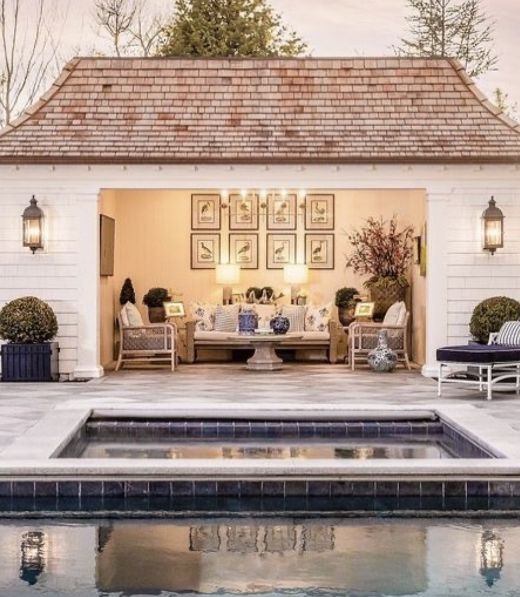 white pool house with cedar shake roof and cozy lounge seating overlooking pool