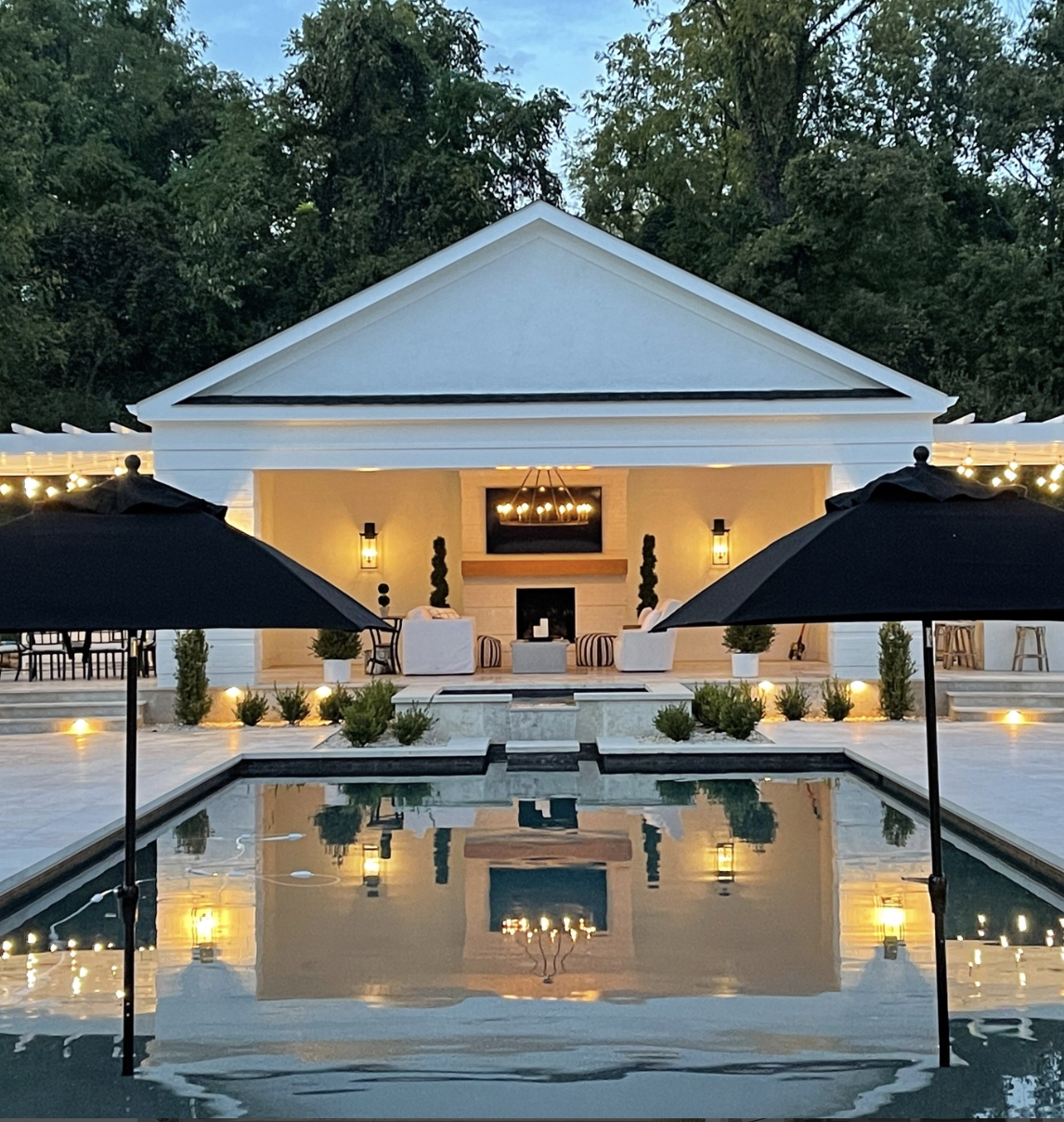 classic white pool house with black patio umbrellas and swimming pool reflection at dusk