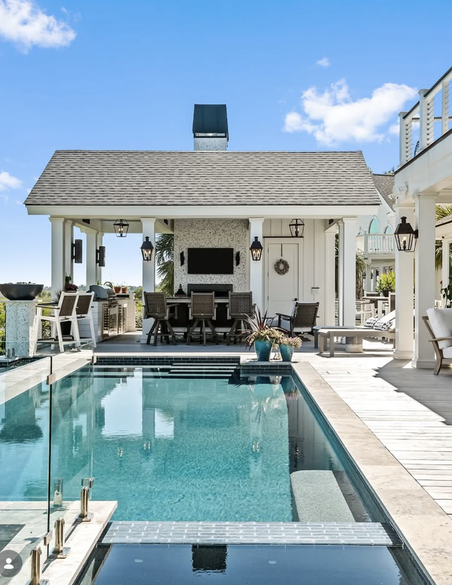 coastal style pool house with white columns, outdoor kitchen, and swimming pool with clear blue water