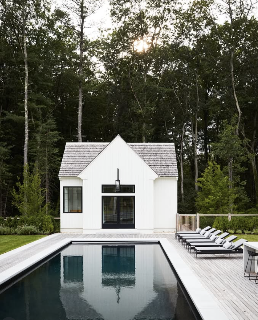 modern farmhouse white pool house with black windows and rectangular backyard swimming pool