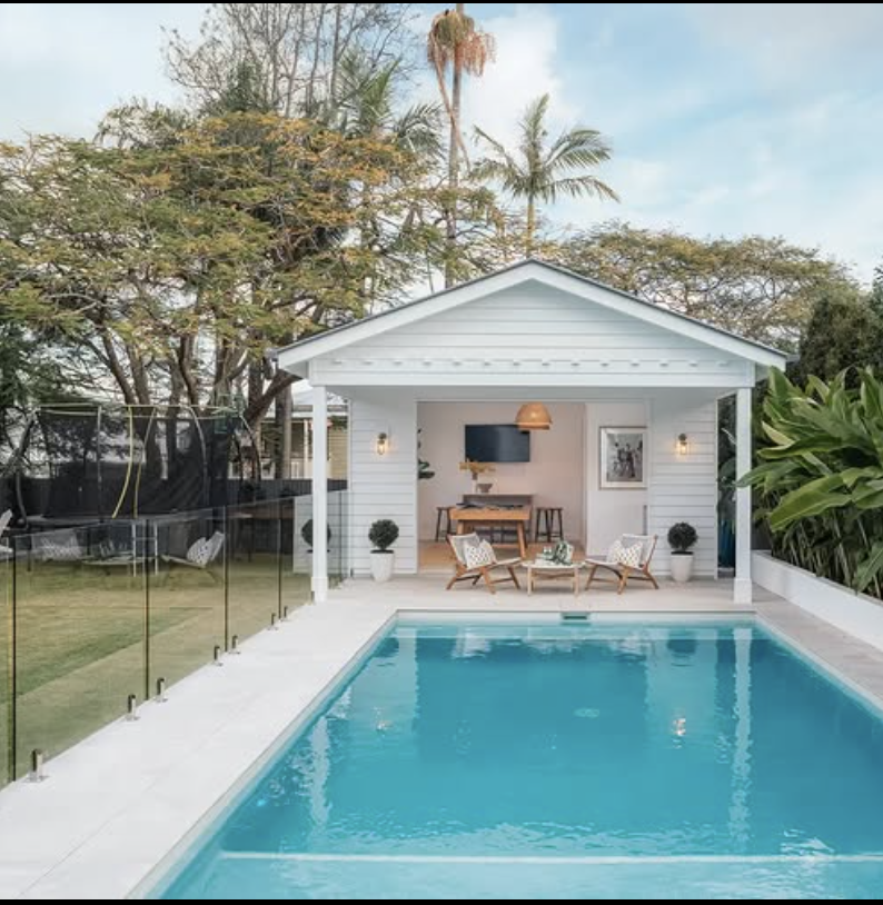small white coastal pool house with open front patio and rectangular backyard swimming pool