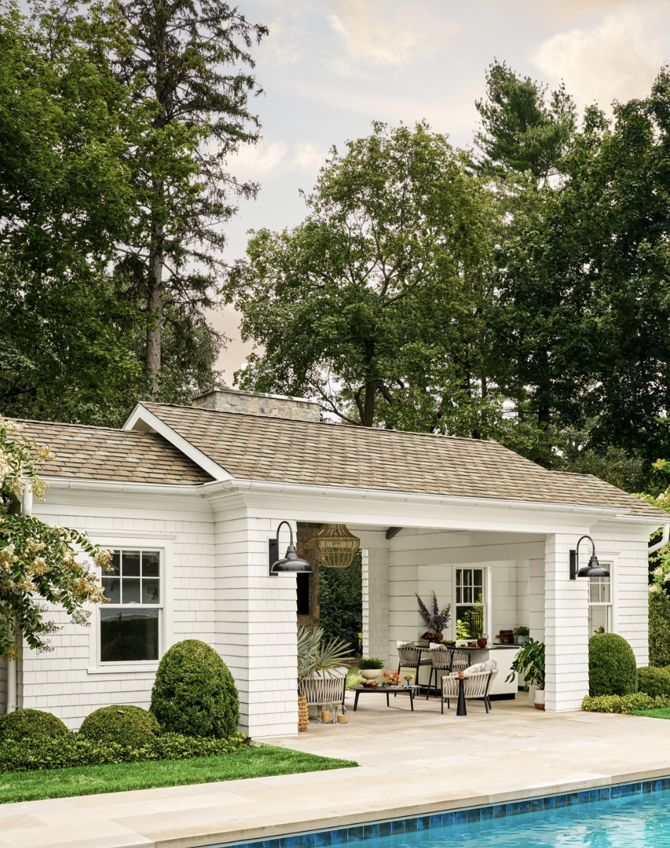 white shingle pool house with covered patio and outdoor seating beside backyard swimming pool