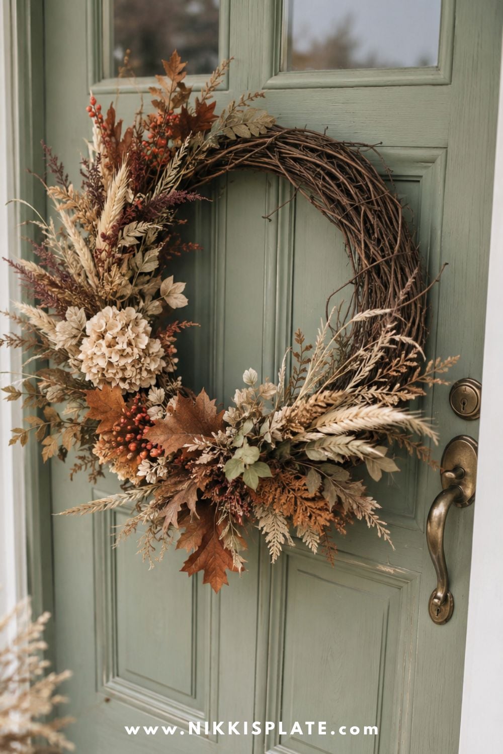 Sage green front door decorated with an asymmetrical fall wreath made from dried grasses, berries, leaves and cream flowers.