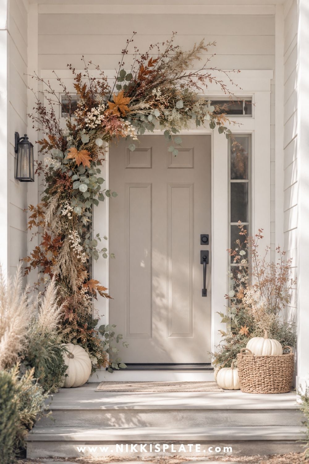 Neutral front door framed with an airy fall garland of rust leaves, eucalyptus, berries and dried grasses.