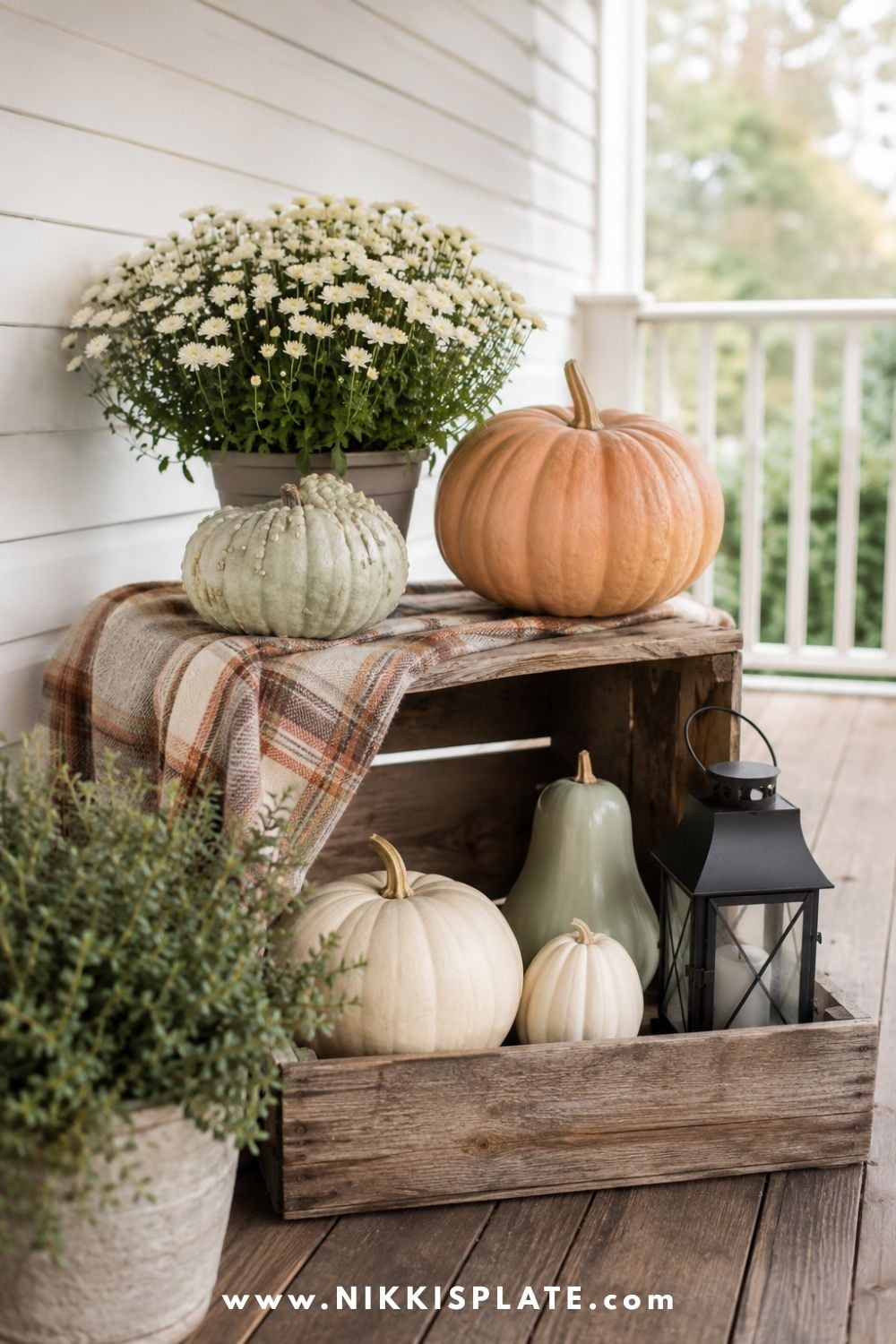 Wooden crates styled with cream pumpkins, sage gourds, a potted mum and a black lantern on a fall porch.