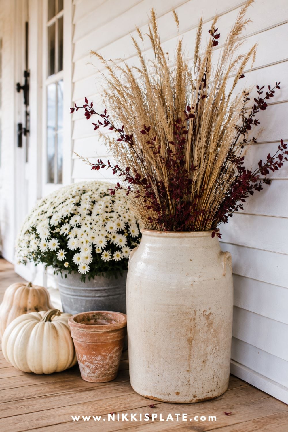 Vintage cream crock filled with dried grasses and wheat, styled with mums, terracotta pots and pale pumpkins.