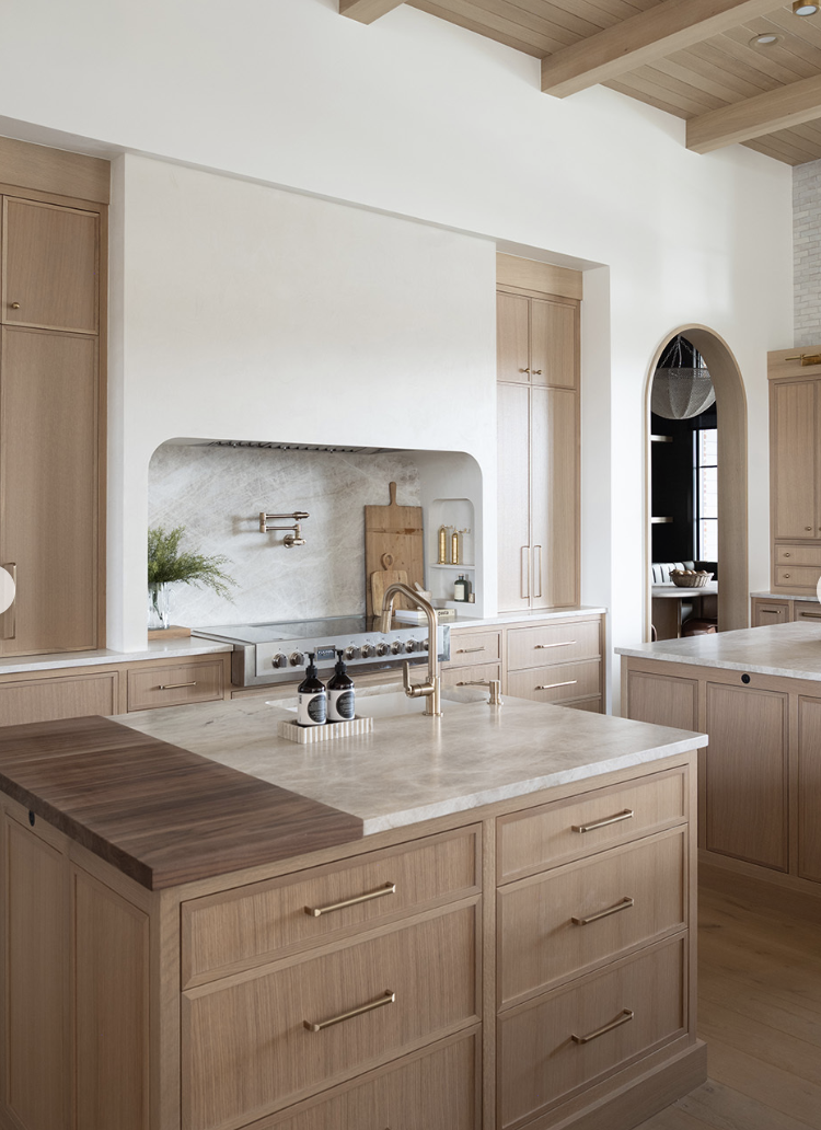 white oak kitchen with arched niche, marble countertops, and warm wood cabinets