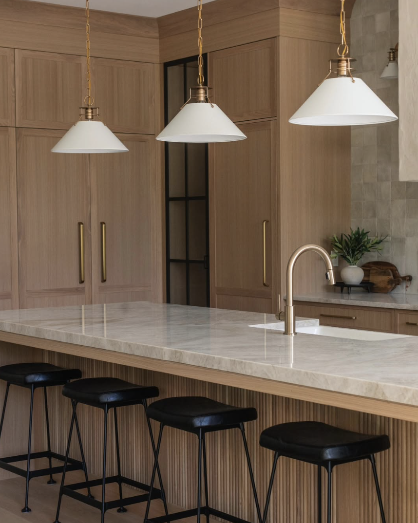 white oak kitchen with fluted island, brass pendant lights, and marble countertops