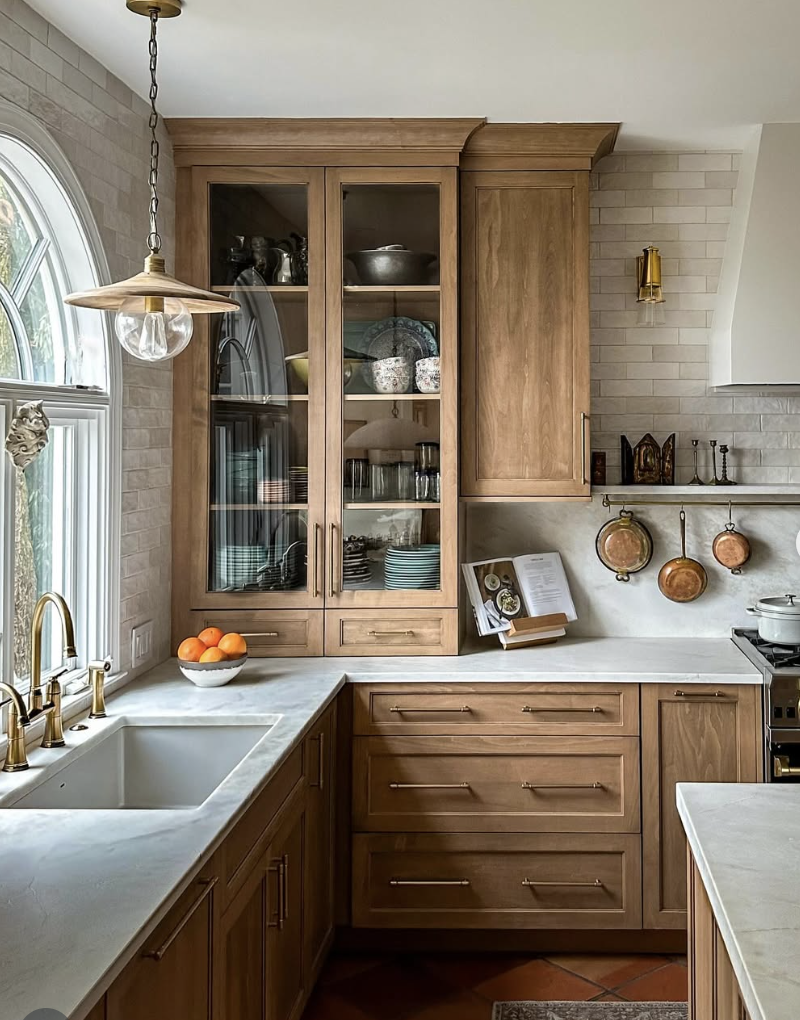 white oak kitchen with glass front cabinets, brass hardware, and marble countertops