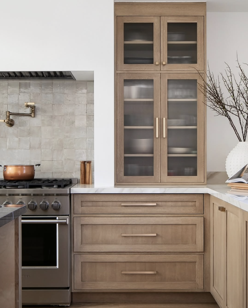 white oak kitchen with glass front cabinets, marble countertops, and warm wood cabinetry