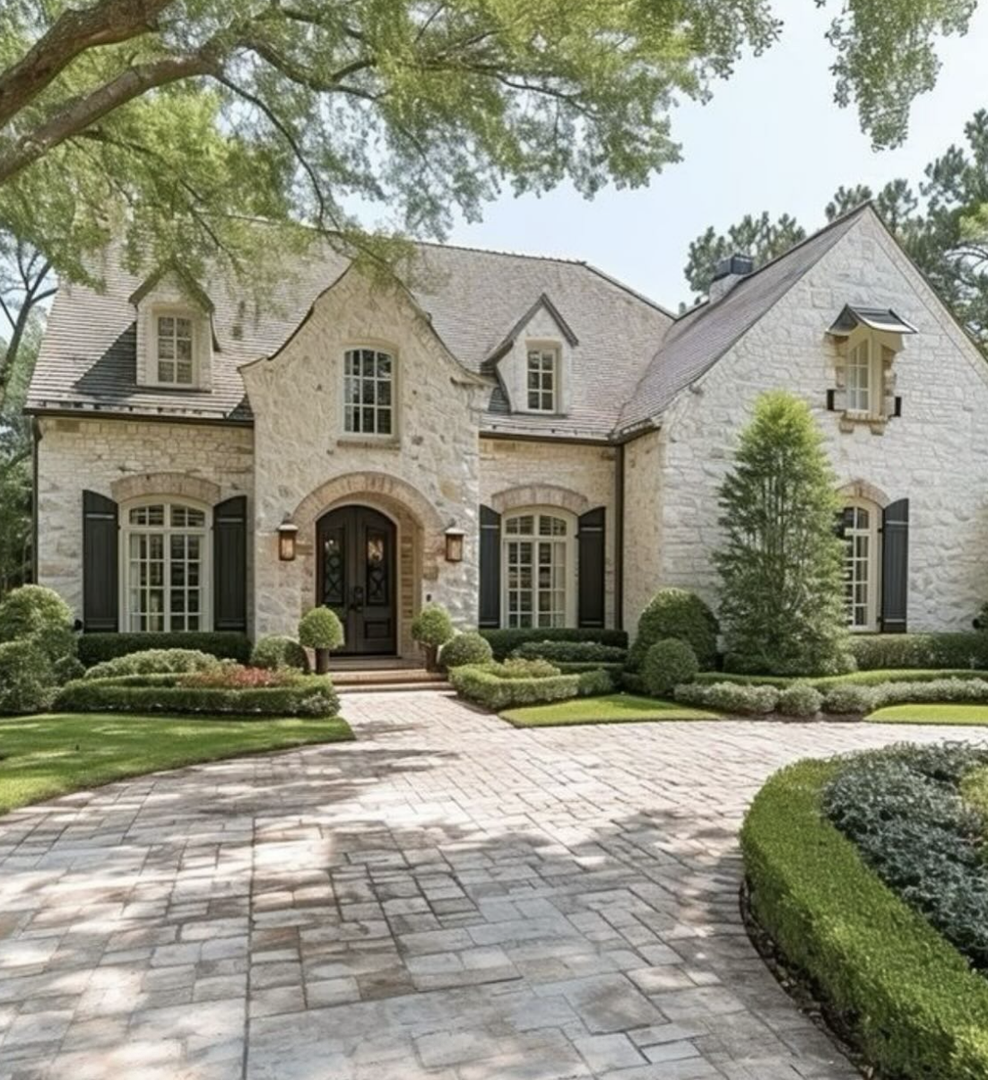 Landscaping ideas for front of house featuring European stone exterior, structured boxwood hedges, manicured lawn, and paver driveway.