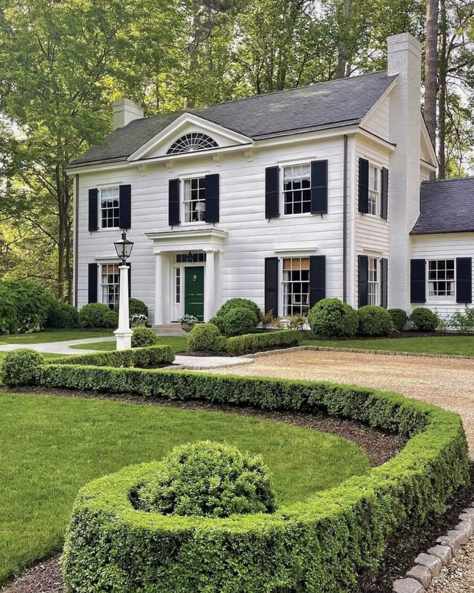Landscaping ideas for front of house featuring formal boxwood hedges, manicured lawn, and symmetrical colonial-style exterior.