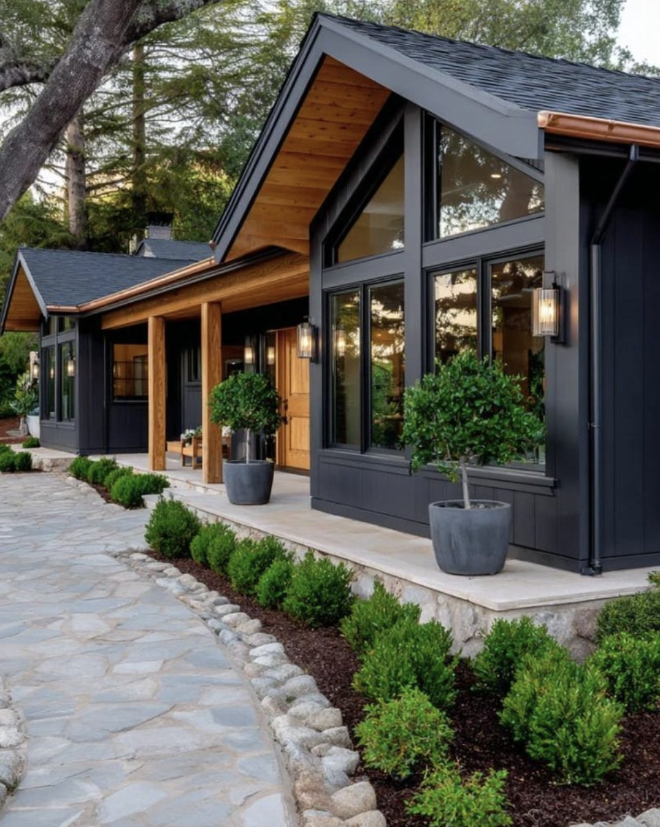 Landscaping ideas for front of house featuring a modern black exterior, stone walkway, potted trees, and structured boxwood shrubs.