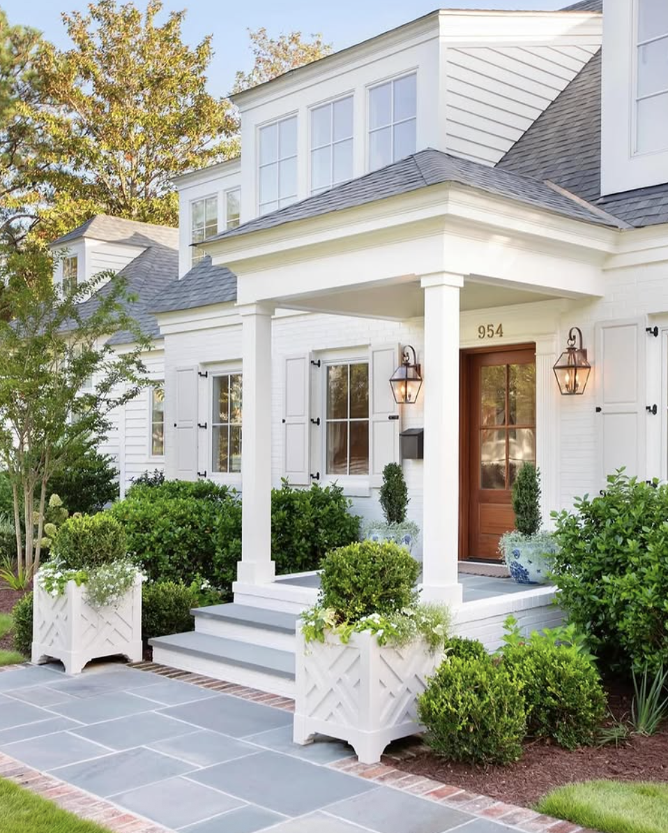 Landscaping ideas for front of house featuring a modern farmhouse porch with structured shrubs, white planters, and lantern sconces.