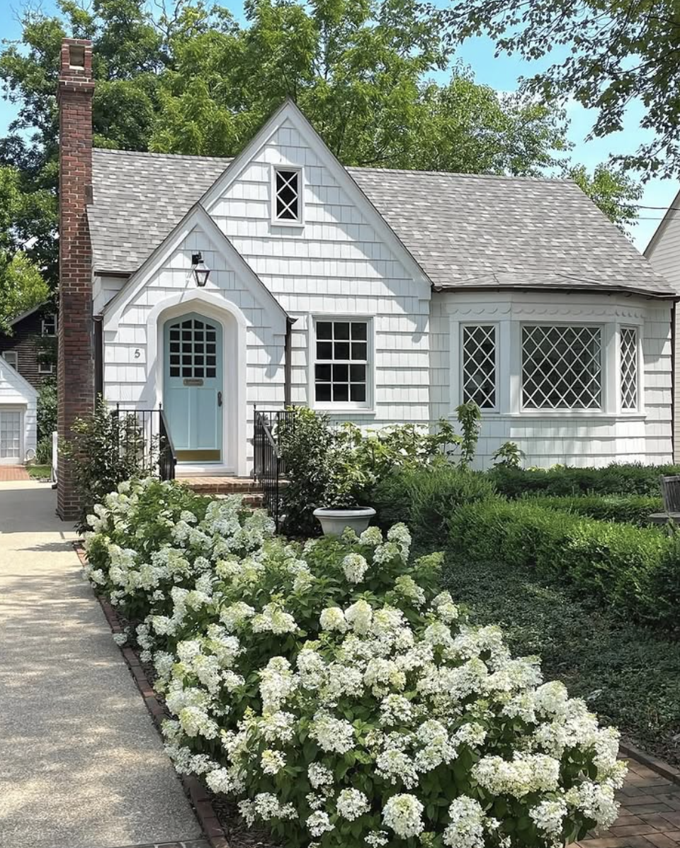 Landscaping ideas for front of house featuring a white cottage exterior with hydrangea-lined walkway and manicured hedges.