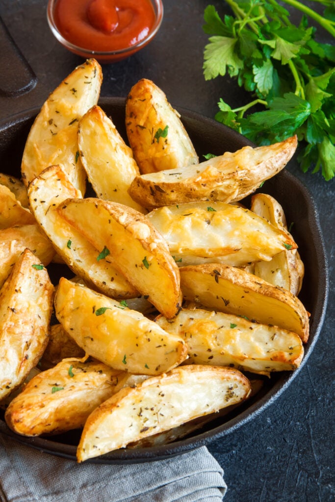 Baked potato wedges with cheese and herbs and tomato sauce on black background - homemade organic vegetable vegan vegetarian potato wedges snack food meal. - 10 Easy Campfire Recipes (Be the Master of Campfire Cooking); Here are 10 campfire cooking recipes to try this summer!