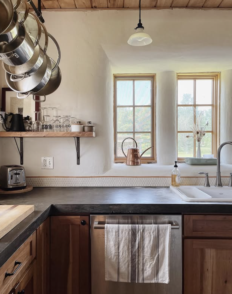 Farmhouse kitchen with dark concrete countertops, wood cabinets, open shelving, and copper accents.