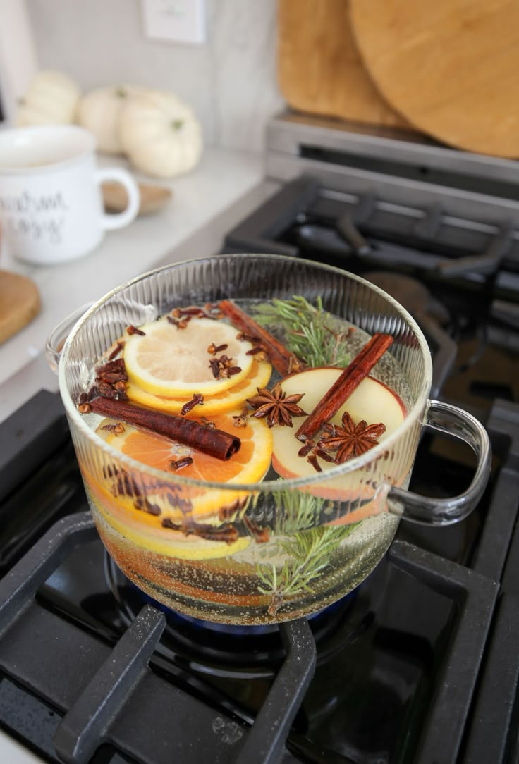 Glass simmer pot on stove filled with cinnamon sticks, orange slices, apple slices, star anise, and rosemary for a natural fall home fragrance.
