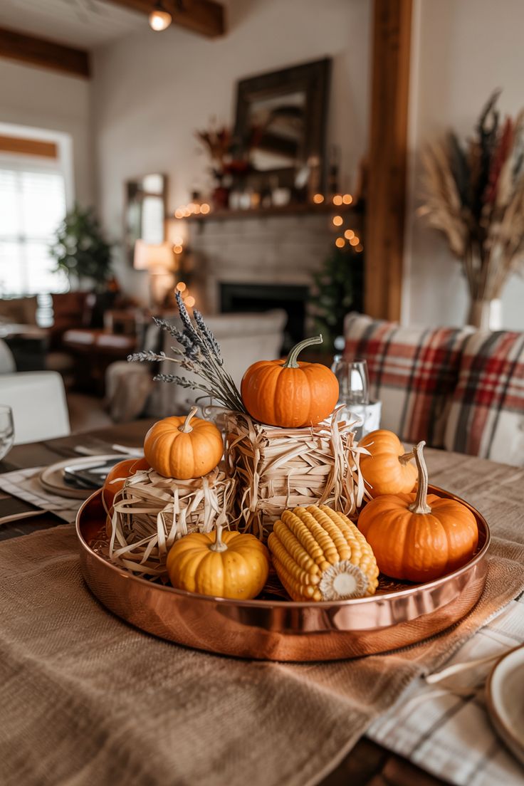 Budget-friendly fall table centerpiece with mini pumpkins, corn, hay bales, and lavender in a copper tray on a neutral table runner for a cozy autumn look.