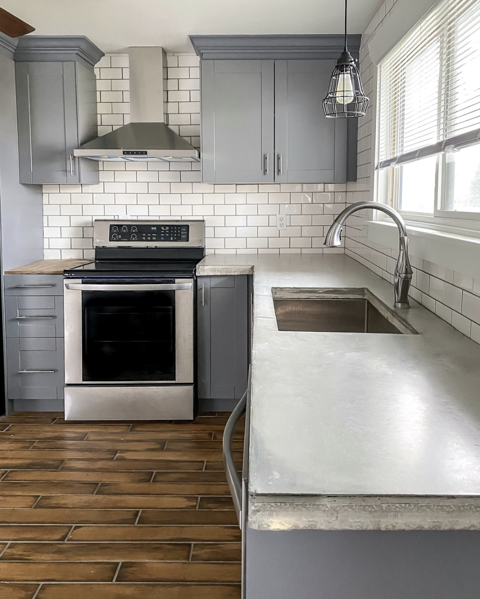 Modern kitchen with gray cabinets, subway tile backsplash, concrete countertops, and stainless steel appliances.