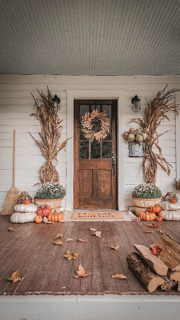 Farmhouse porch decorated for fall with layered rugs, a natural wreath, pumpkins, corn stalks, and cozy autumn details for a welcoming entryway.