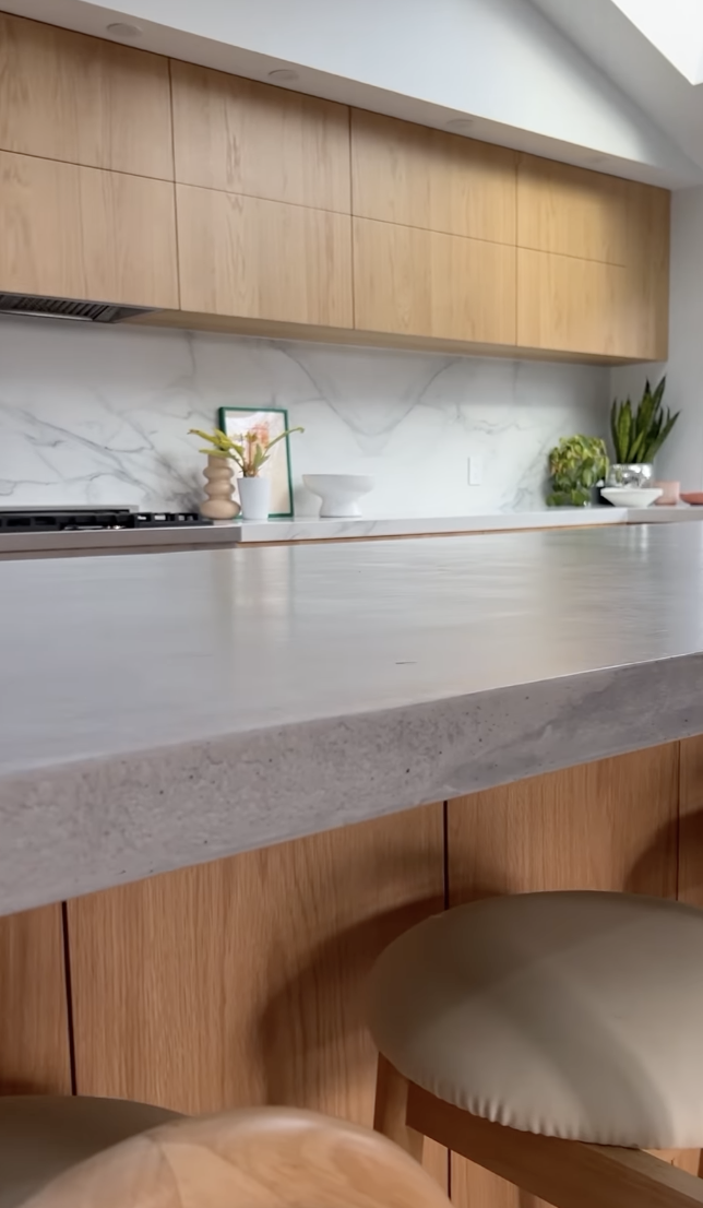 Modern kitchen with light wood flat-panel cabinets, gray concrete countertops, and marble backsplash.