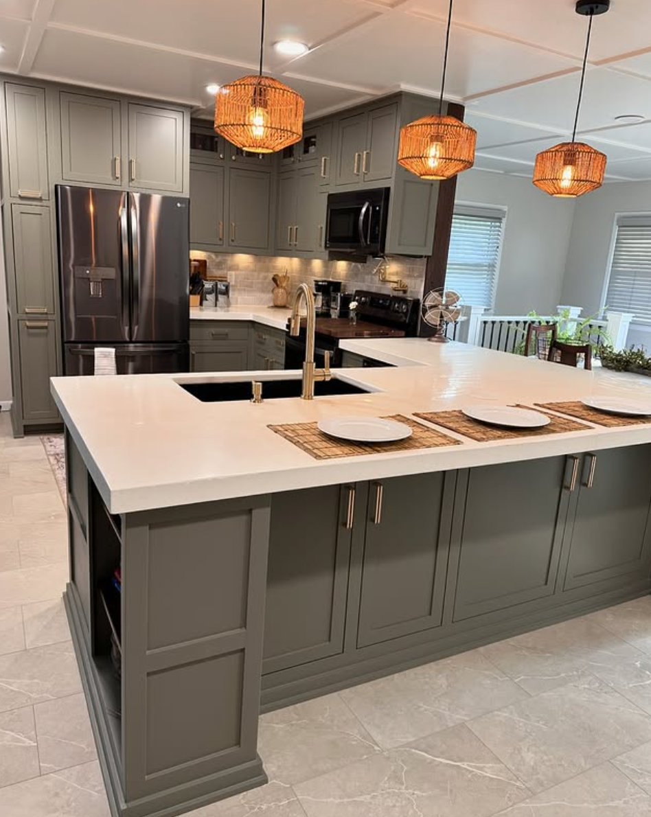 Elegant kitchen with olive green cabinets, white countertops, gold faucet, and warm rattan pendant lights over a large island.
