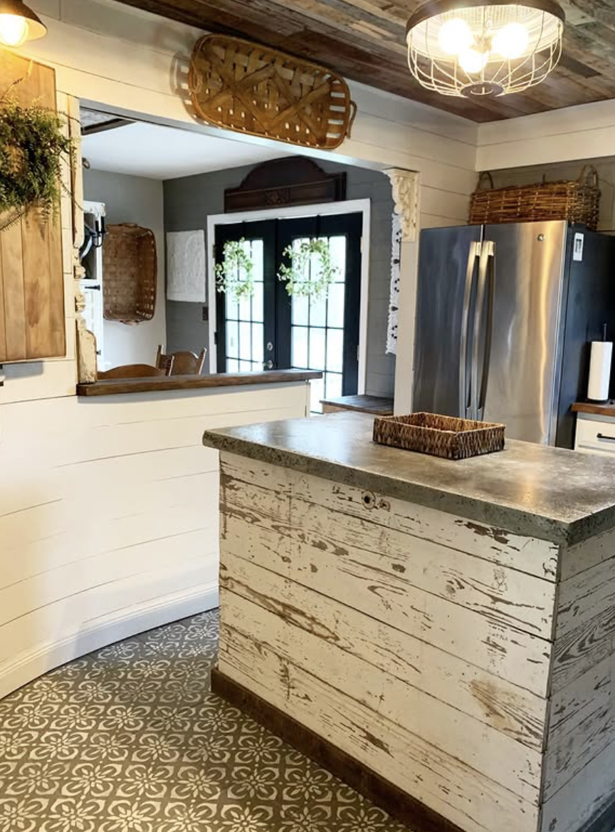 Rustic farmhouse kitchen with a distressed shiplap island and gray concrete countertop, featuring patterned tile flooring and cozy country decor.