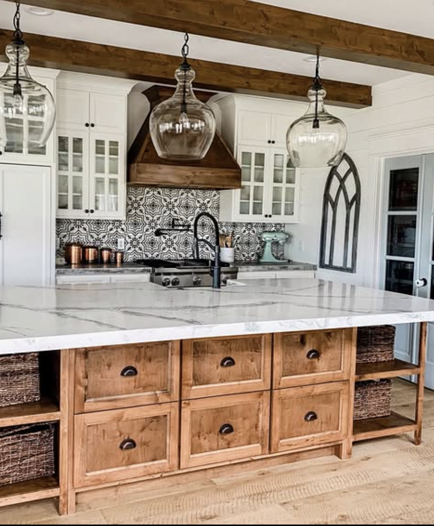 Farmhouse kitchen with wood beams, patterned tile backsplash, wood island base, and light concrete countertops.