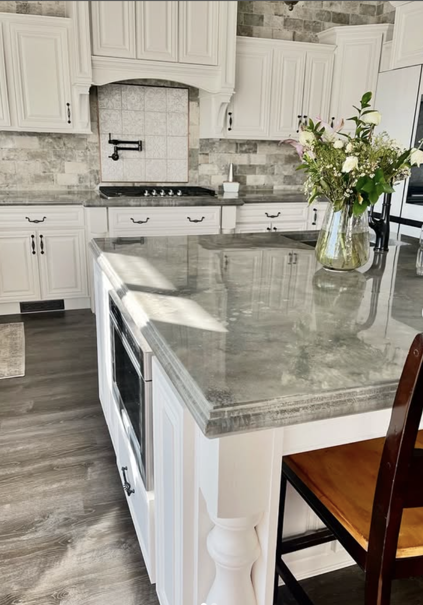 Classic white kitchen with raised panel cabinets, polished gray concrete countertops, and stone backsplash.