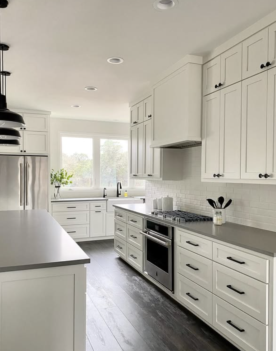 Bright white shaker kitchen with smooth gray concrete countertops, black hardware, and stainless steel appliances.