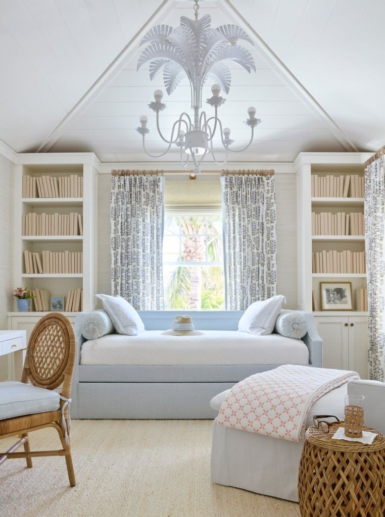 Coastal office with daybed centered between built-in bookshelves, featuring vaulted ceiling, soft blue upholstery, patterned curtains, and woven accents.