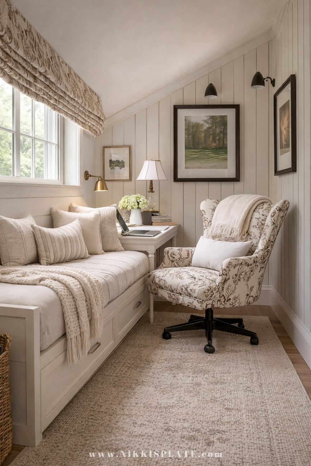 Cozy home office with daybed under a sloped ceiling featuring a floral desk chair, neutral bedding, brass lighting, and layered farmhouse decor.