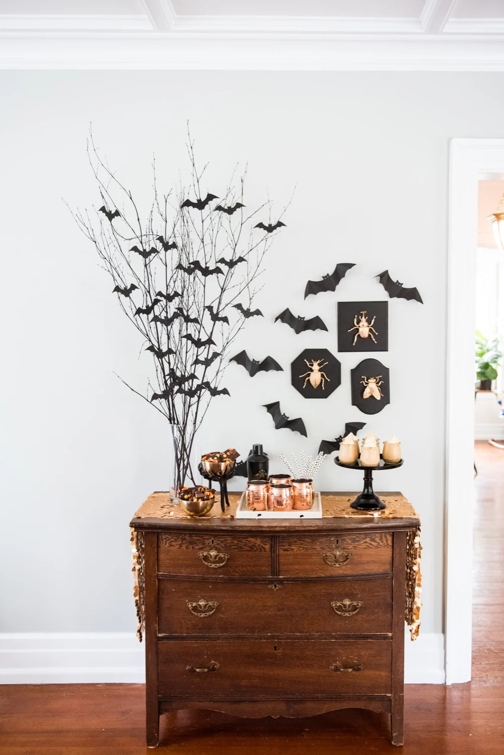 DIY Halloween centerpiece with tall branches covered in black bat cutouts and spooky wall art.