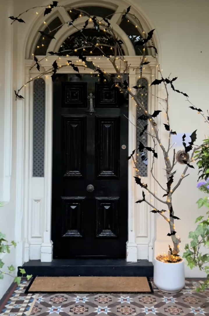 Black front door framed with branches wrapped in lights and covered with flying Halloween bat decorations.