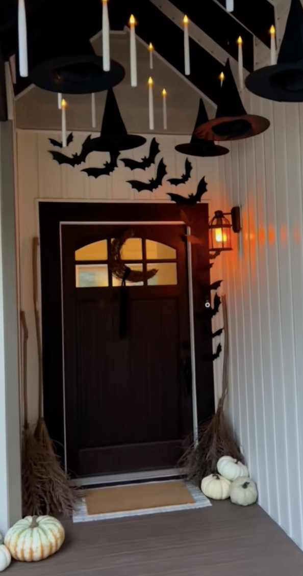 Front porch decorated with flying Halloween bat decorations, floating witch hats, glowing candles, and pumpkins.