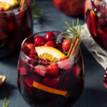 Red Christmas Sangria Recipe; made with red wine, brandy cranberry pomegranate juice, sparkling apple cider and fruit. Topped with cinnamon sticks and rosemary to garnish