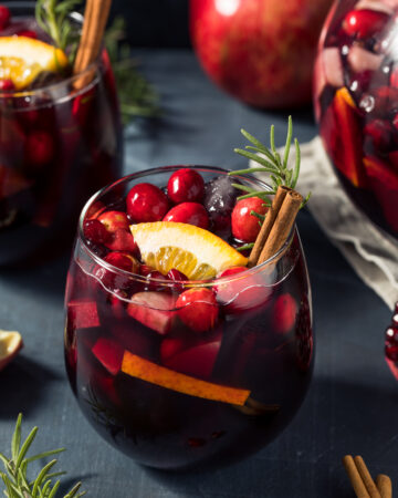 Red Christmas Sangria Recipe; made with red wine, brandy cranberry pomegranate juice, sparkling apple cider and fruit. Topped with cinnamon sticks and rosemary to garnish