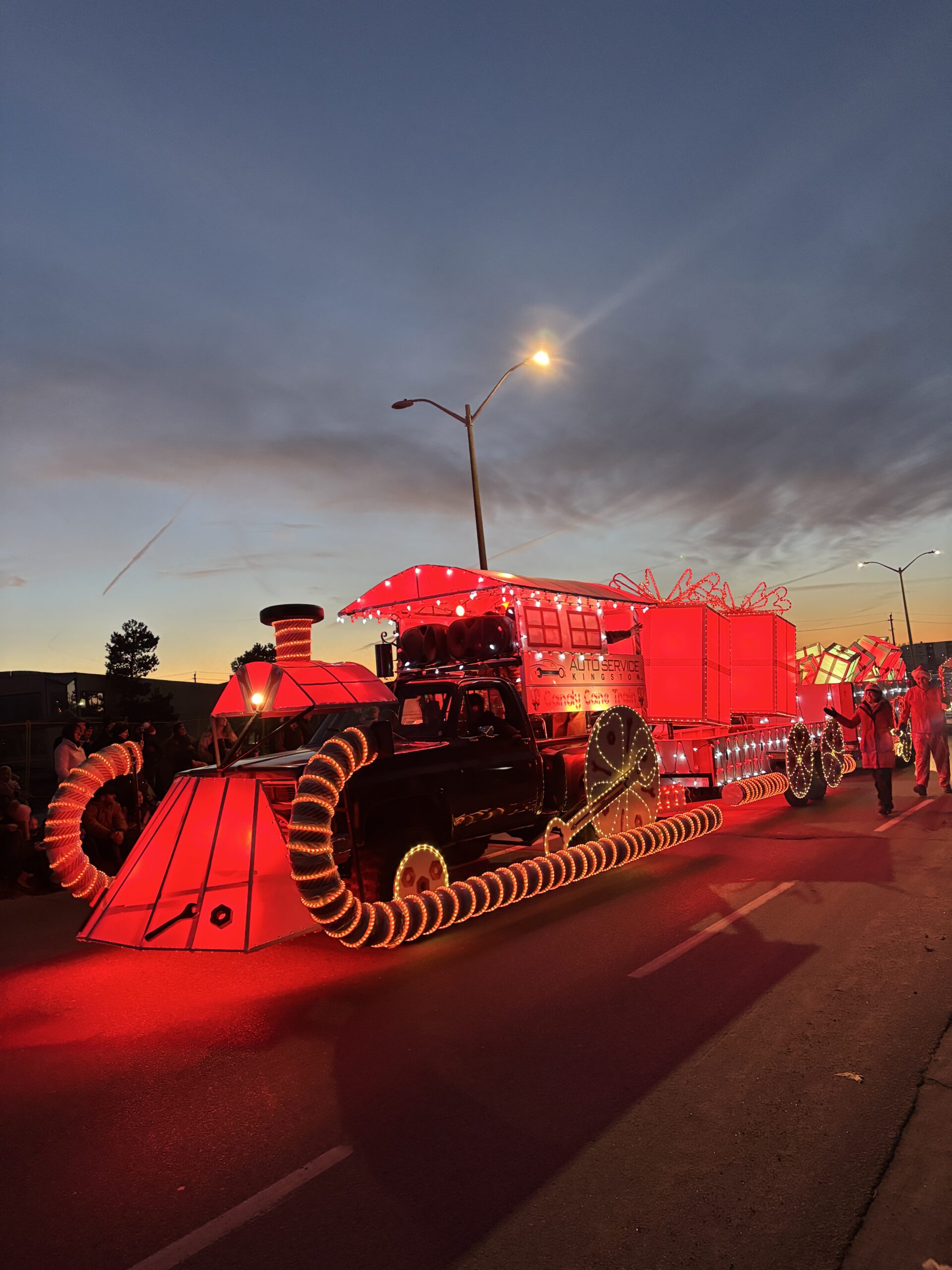 Candy cane-themed Christmas parade float designed as a glowing red train with illuminated wheels and curved candy cane details.