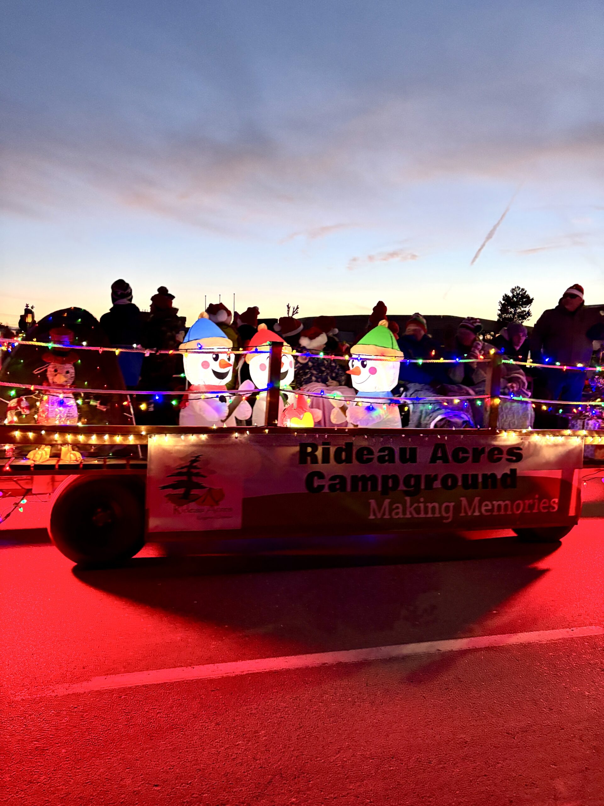 Christmas parade float decorated with glowing snowman characters, colorful string lights, and a Rideau Acres Campground sign.