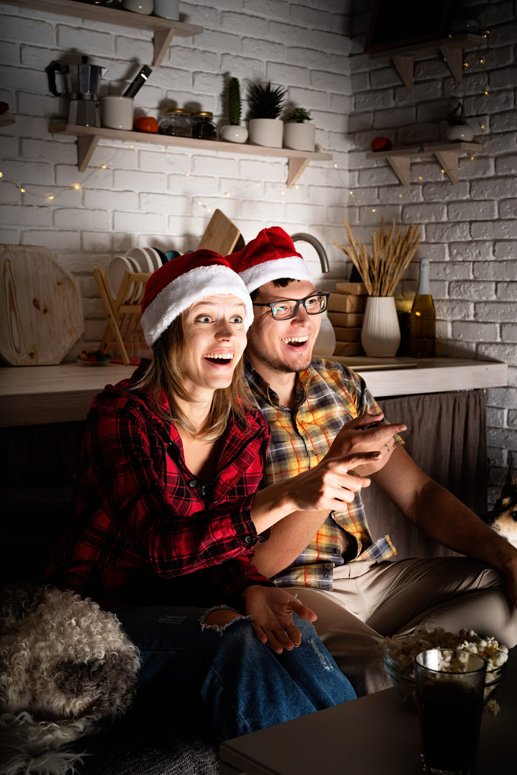 How to Embrace the Festive Cheer; Movie night. Young couple watching movies at home at christmas pointing to the screen eating popcorn