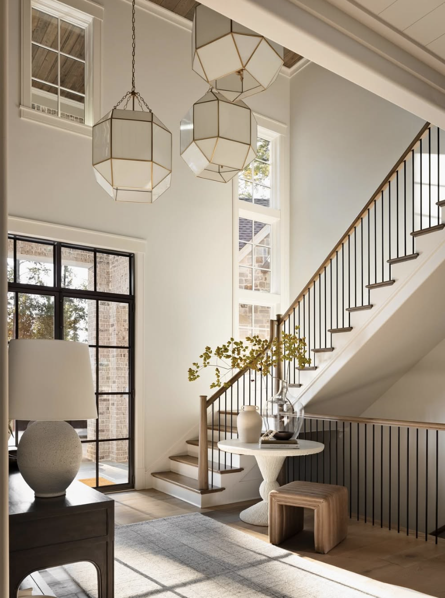 Geometric pendant chandelier hanging in a two-story foyer with staircase, iron railings, natural wood accents, and modern entry decor